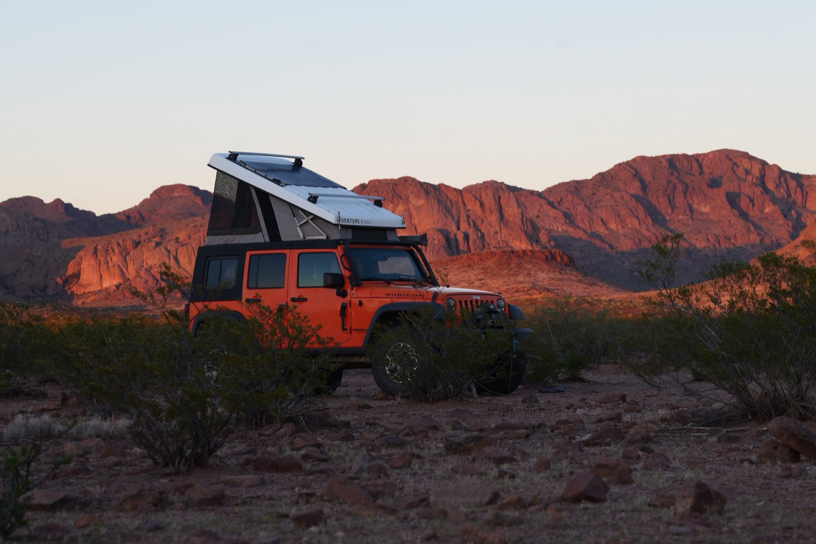 Orangie with the Ursa Minor camper open at sunset below red rock mountains